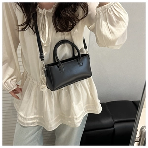 Detail of minimalist black leather crossbody bag with silver hardware on a model