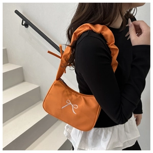 Detail of orange nylon shoulder bag featuring white bow embroidery and ruffled strap design