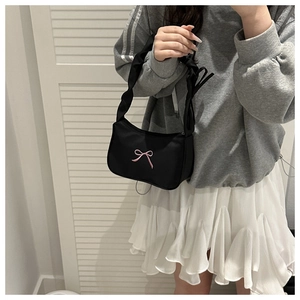 Detailed view of black bow-knot underarm bag held by model wearing a pleated skirt