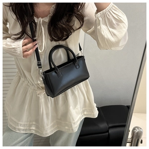 Detail shot of a black PU leather handbag showing top handles and adjustable shoulder strap