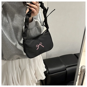 Detail of black pleated shoulder bag featuring a pink ribbon bow embroidery and scrunchie strap