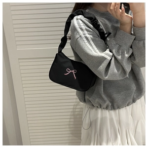 Detail of black underarm bag featuring pink bow embroidery and ruffled shoulder strap