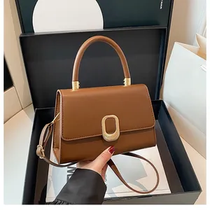 Detail of a brown leather handbag with a gold oval buckle placed in a luxury gift box