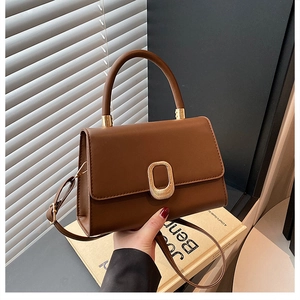 Detail of dark brown leather handbag with gold oval clasp and adjustable shoulder strap