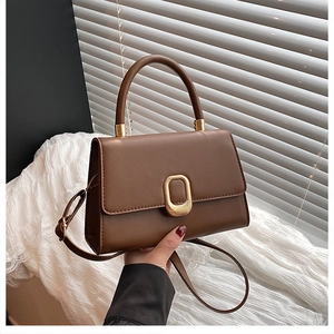 Detail of brown leather handbag featuring a golden oval clasp and curved handle