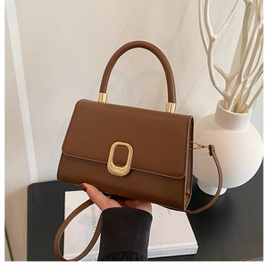 Close-up of caramel brown leather handbag with golden oval metal buckle and top handle