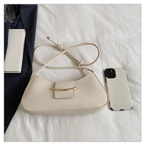 Detail view of a minimalist beige leather baguette bag with a stylish gold metal buckle bar