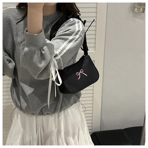 Close-up of black nylon shoulder bag with a pink satin bow accent on a model