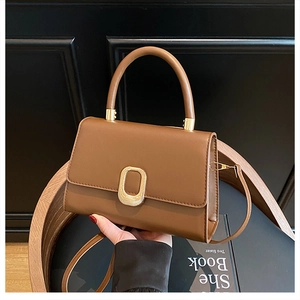 Detail view of brown leather handbag with gold oval buckle and cylindrical top handle
