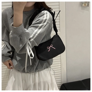 Detail of black shoulder bag with pink bow embroidery worn with a stylish outfit