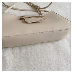 Detail of a creamy white half-moon underarm bag with an elegant gold metal clasp