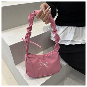 Detail of pink nylon shoulder bag with ruffled handle and bow embroidery on light background