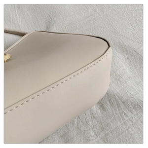 Detailed close-up of cream leather shoulder bag with precision stitching and gold buckle