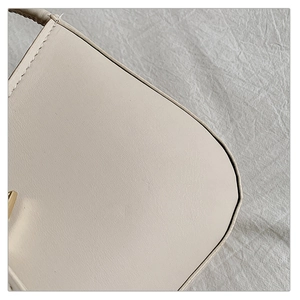 Macro detail of creamy leather texture and fine stitching on a stylish crossbody bag