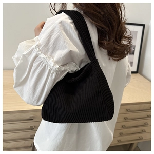 Detail of black corduroy shoulder bag with striped texture worn on a white shirt