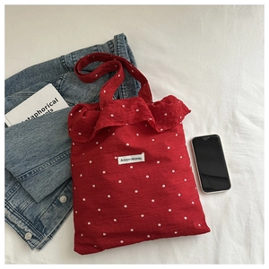 Detail of red floral tote bag with ruffle trim and AGOGO label on white bedding