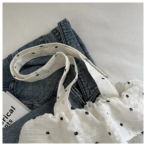 Close-up of white seersucker fabric with black floral embroidery on a ruffled handbag