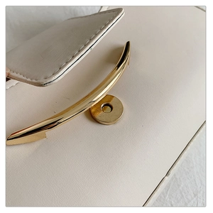 Detail of cream leather handbag with curved gold metal handle and magnetic snap closure