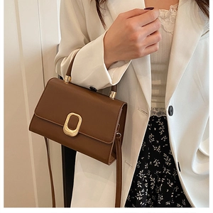 Detail of a brown leather crossbody bag with a gold buckle on a white blazer outfit