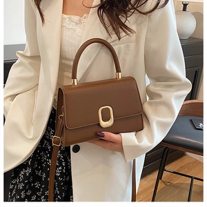 Detail of a dark brown crossbody square bag with metal clasp shown on a white blazer
