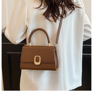Close-up of a dark brown leather crossbody bag with an oval gold metal buckle