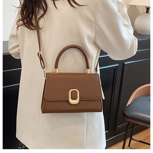 Detail of a brown leather crossbody bag featuring a golden oval metal lock and top handle