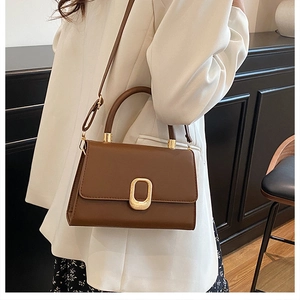 Detail of a dark brown crossbody bag with a gold oval lock and textured leather finish