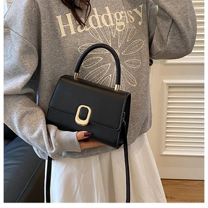 Detail of minimalist black square bag with a textured golden oval metal lock clasp