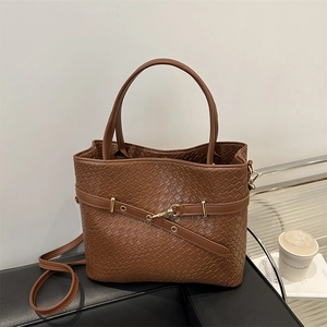 Détail du sac cabas marron tissé avec ferrures dorées sur un canapé