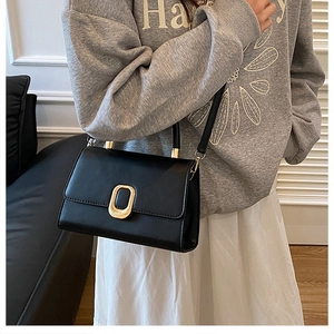 Detail view of black minimalist leather crossbody bag with oval gold clasp on a model