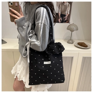 Close-up of black floral tote bag with white ruffles and branded logo tag detail