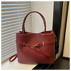 Détail du sac cabas rouge avec texture tressée et boucles dorées sous lumière naturelle