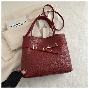 Détail de la texture en cuir tressé d'un sac cabas bordeaux avec boucle métallique d'or