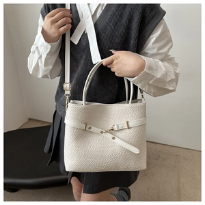 Gros plan du sac seau blanc à motif crocodile et détails dorés porté par un mannequin