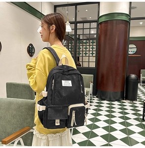 Détail d'un sac à dos noir de style collège avec poches et sangles blanches réglables