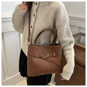 Détail du sac seau marron foncé à texture tressée avec bandoulière et boucles en métal