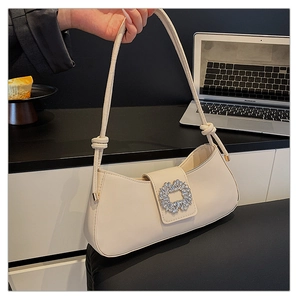 Détail du sac baguette crème avec boucle en strass et bandoulière à nœuds