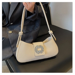 Gros plan sur la boucle en strass étincelante et la bandoulière nouée du sac crème