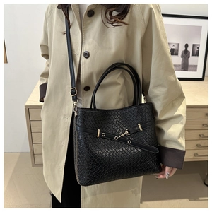 Détail d'un sac seau noir tissé avec anneau doré porté sur un trench-coat kaki