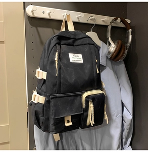 Détail du sac à dos en nylon noir avec sangles crème et poches à boucles avant