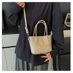 Detail of a beige PU leather tote bag with dual handles and gold-tone hardware on a desk