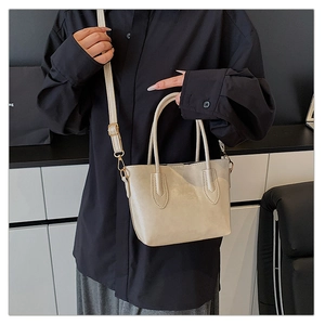 Detail of cream tote bag featuring cylindrical handles and detachable gold hardware straps