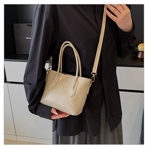 Detailed view of beige tote bag handles and gold hardware worn by a model in black shirt