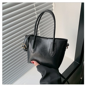 Close-up of black leather tote bag with golden metal buckles and adjustable strap