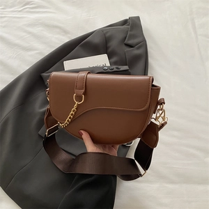 Detail of dark brown saddle bag with gold metal chain and wide nylon shoulder strap
