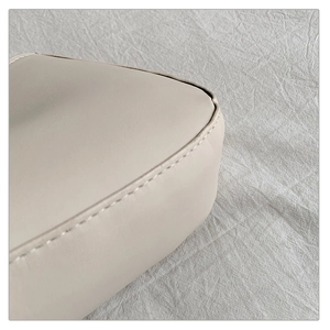 Détail de couture raffinée et texture cuir crème premium sur le sac sous l'aisselle