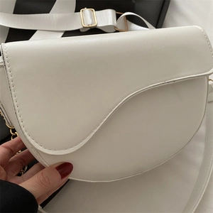 Detailed close-up of white saddle bag showing matte leather texture and gold buckle