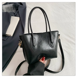 Close-up of black leather tote bag with fine texture, dual handles and long shoulder strap