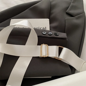 Detail of adjustable white woven strap with shiny gold buckle on a gray blazer