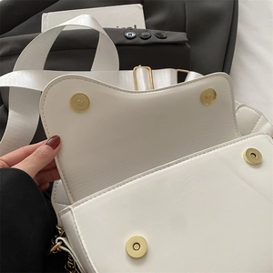 Detail of white saddle bag interior with dual gold magnetic clasps and wide woven strap